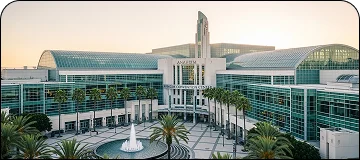 Modern exterior of Anaheim Convention Center with large glass facade, palm trees, and event banners for LGB to Anaheim Convention car service.