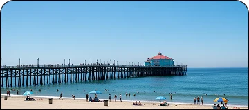 Sunny beach scene at Huntington Beach with ocean people, waves, surfers, and the iconic pier in the background for LGB to Huntington Beach car service.