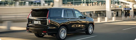 Rear side view of a black Cadillac Escalade in fast motion with blur effect on its wheels and background.