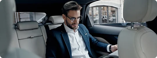 A business traveler in a navy suit reviews documents in the backseat of a luxury sedan with soft beige leather interiors.