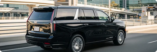Rear view of a black Cadillac Escalade in fast motion passing through a city area where the background and the wheels of the car are in blur motion.