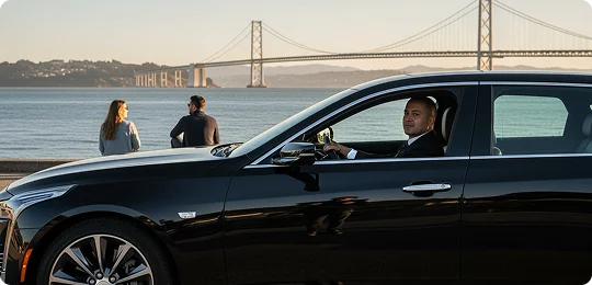 A side profile of a black luxury sedan (appears to be a Cadillac) is shown with a chauffeur in the driver's seat looking out and smiling. The car is parked near a waterfront. In the background, two individuals sit by the water enjoying the view of the San Francisco-Oakland Bay Bridge under the warm light of sunset or sunrise.
