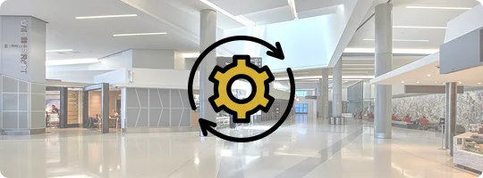 A yellow gear icon surrounded by two black circular arrows (representing seamless processing or system integration) overlaid on a blurred image of a brightly lit, modern airport terminal or large lobby.