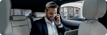 A man smiling on a phone call while riding in a premium sedan.