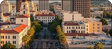Scenic evening view of Riverside with city buildings and main road with minimal traffic and parked cars along with palm trees visible.