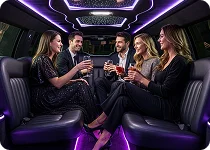 An interior view of a limousine with three women dressed and two men in formal or party attire seated on the dark leather benches, socializing under purple ambient lighting.